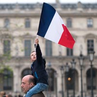Photo d'un père portant sur ses épaules son fils qui tient un drapeau français deavnt le Musée du Louvre, lors de la victoire d'Emmanuel Macron aux élections présidentielles françaises de 2017 - Flickr 34527195605