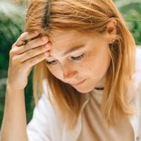 Photo en couleur d’une jeune femme rousse concentrée sur une facture se tenant la tête d'une main avec un stylo entre les doigts - Pexels 8927472