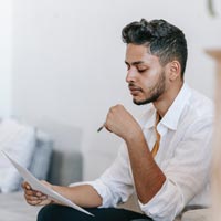 Photo en couleur d’homme concentré lisant des documents et travaillant sur un ordinateur portable - Pexels 7128988
