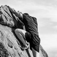 Photo en N/B d’un homme en tenue de sport escaladant la pointe d'un rocher - Pexels 6659108