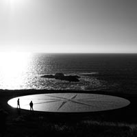 Photo en noir et blanc de 2 personnes marchant sur une boussole géante au bord d'une plage - Pexels 8546334