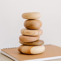 Photo en couleur d’une pile de galets en bois posés en équilibre sur des cahiers sur un bureau - Pexels 8250990