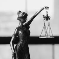 Photo N/B d’une petite statue de Lady Justice posée sur un bureau devant une fenêtre - Pexels 6077099