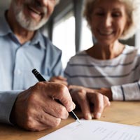 Photo en couleur d'un couple de personnes agées souriantes signant un contrat sur un bureau avec un stylo-bille - iStockPhoto 1226093733