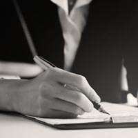 Photo en N/B d’une femme en tailleur noir et blanc écrivant sur un bureau avec un stylo plume doré sur un porte-bloc - iStock-1137879756